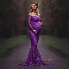 A pregnant woman wears a long-sleeved, off-the-shoulder purple lace mermaid maternity gown.