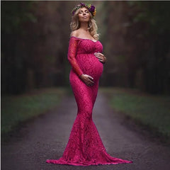 A pregnant woman wears a long-sleeved, off-shoulder magenta lace mermaid maternity gown.