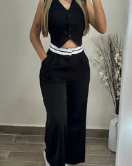 A woman wears a black sleeveless buttoned vest and matching high-waisted pants with white trim.