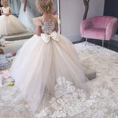 A floor-length flower girl ball gown with a lace bodice, tulle skirt, and a large back bow.