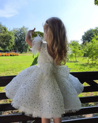 A young girl wears a white sleeveless ball gown with a sequined tulle skirt and feather shoulders.