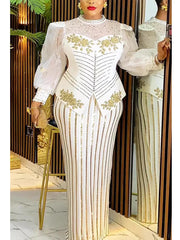 A woman wears a white long-sleeved evening dress with gold sequin stripes and floral embroidery.