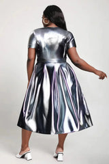 A woman wears a metallic silver short-sleeved midi dress with a pleated A-line skirt.