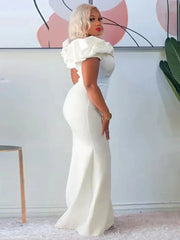 A woman wears a floor-length white mermaid gown with off-the-shoulder ruffled sleeves.