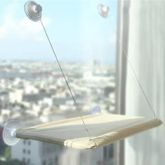 A beige cat hammock suspended by suction cups on a window.