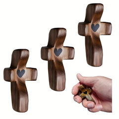 Three wooden pocket crosses with heart-shaped cutouts are displayed alongside a hand holding one.