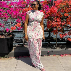 A woman wears a floral print two-piece set featuring a sleeveless pleated top and wide-leg pants.