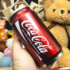 A red Coca-Cola branded stainless steel mug shaped like a soda can held in a hand.