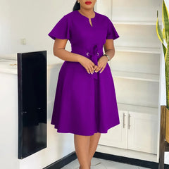 A woman wears a knee-length purple A-line dress with short sleeves and a lace-up waist detail.