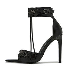 A black stiletto sandal with a pointed open toe, ankle strap, zipper detail, and buckle accents.