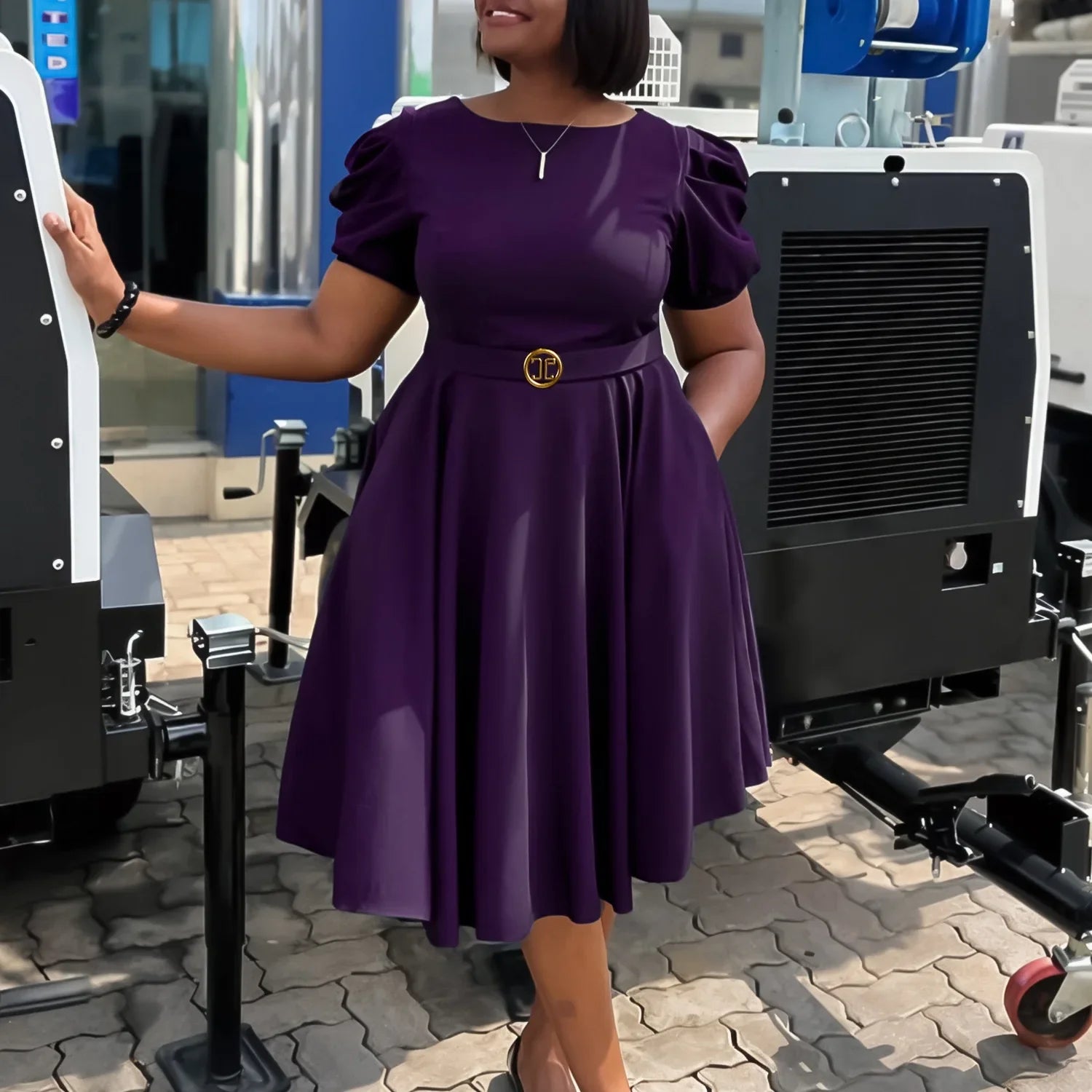 A woman wears a short-sleeved, purple pleated midi dress with a gold-buckled belt.