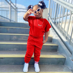 A young girl wears a red short-sleeved t-shirt and matching elastic-waist pants.