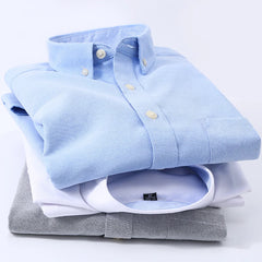 A stack of three men's long-sleeve Oxford shirts in blue, white, and grey.