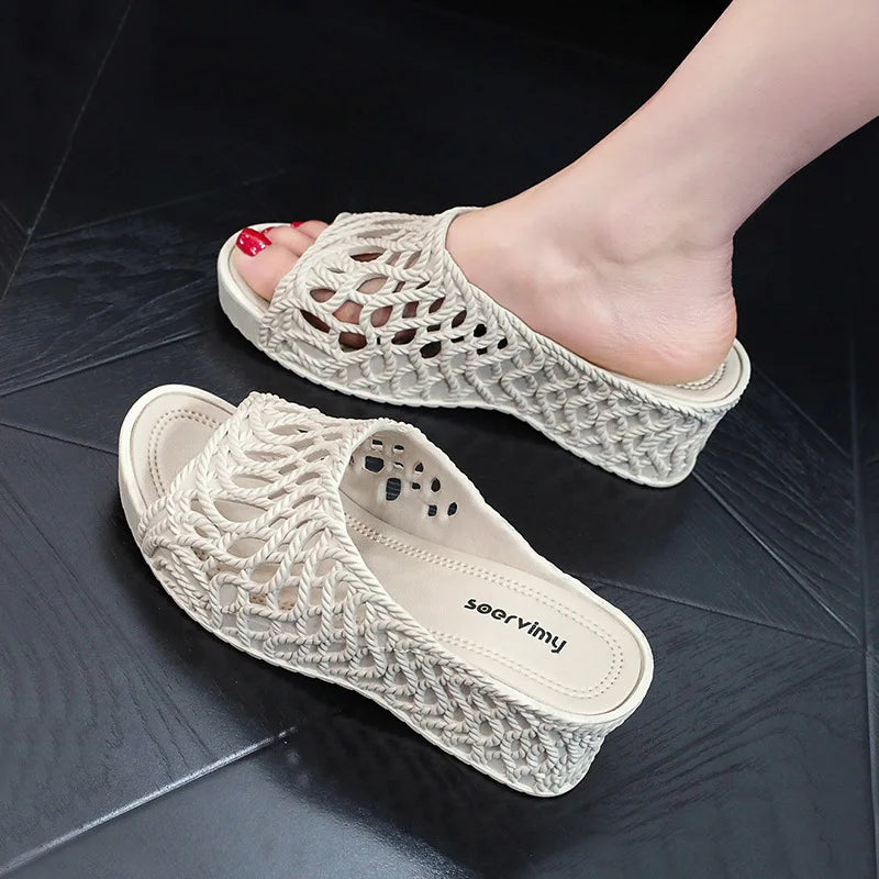 A pair of beige wedge slippers with a hollow-out rope design and a peep-toe front.