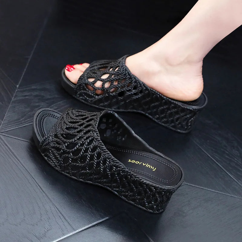 A pair of black wedge slippers with a hollow-out woven upper and a peep-toe design.