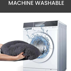 A person holds a round, grey plush pet bed in front of a washing machine.