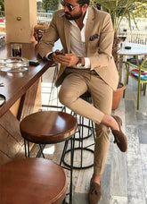 A man wearing a slim-fit beige two-piece suit with a white shirt and brown loafers.
