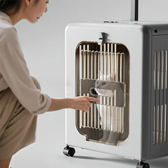 A person touches the door of a portable, white, wheeled pet carrier containing a white cat.