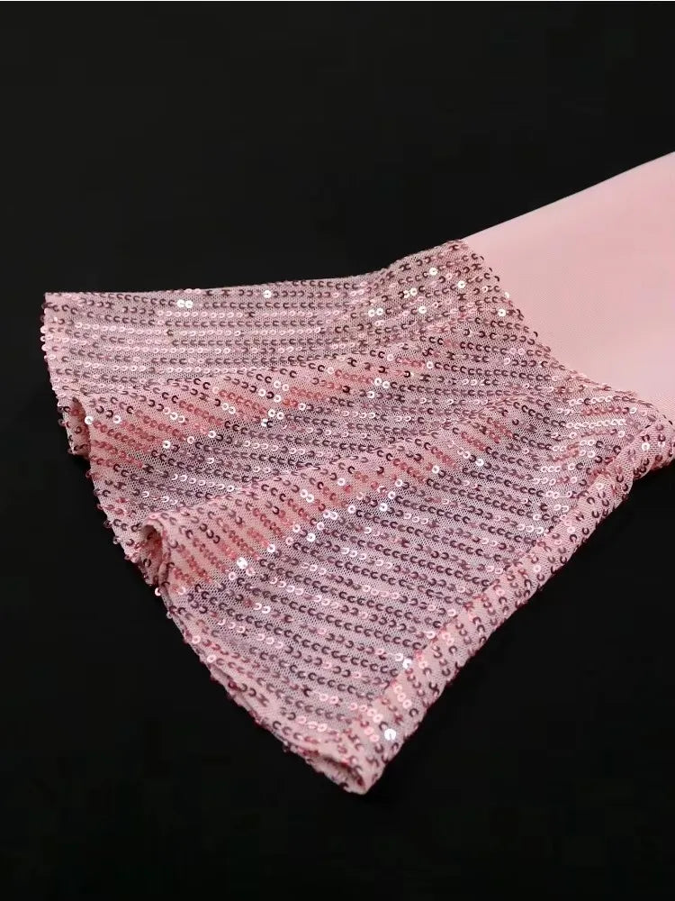 A close-up of a pink long sleeve with a ruffled cuff covered in shimmering sequins.