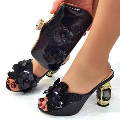 A pair of black peep-toe mules and a matching clutch bag decorated with black floral appliques.