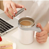 A person holds a white, portable electric mixing mug with a stainless steel interior.