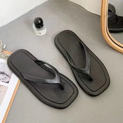 A pair of minimalist black flat flip-flops with a square-toe design.