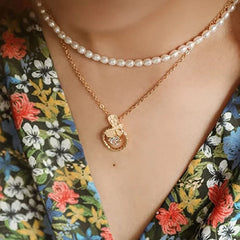 A layered necklace featuring a strand of white oval pearls and a gold chain with a floral pendant.