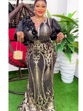 A woman wears a black and gold sequined maxi dress with puff sleeves and a decorative belt.
