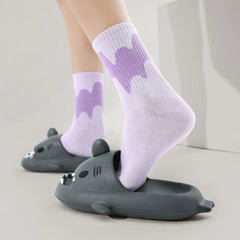 A person wears light purple patterned socks with grey shark-shaped EVA slide sandals.