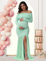 A pregnant woman wears a mint green off-shoulder maternity gown with long sleeves and a side slit.