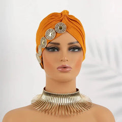 A mustard yellow pleated turban cap decorated with a row of sparkling circular rhinestone accents.