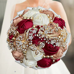 A round wedding bouquet of silk roses in burgundy, champagne, and white with crystal brooches.