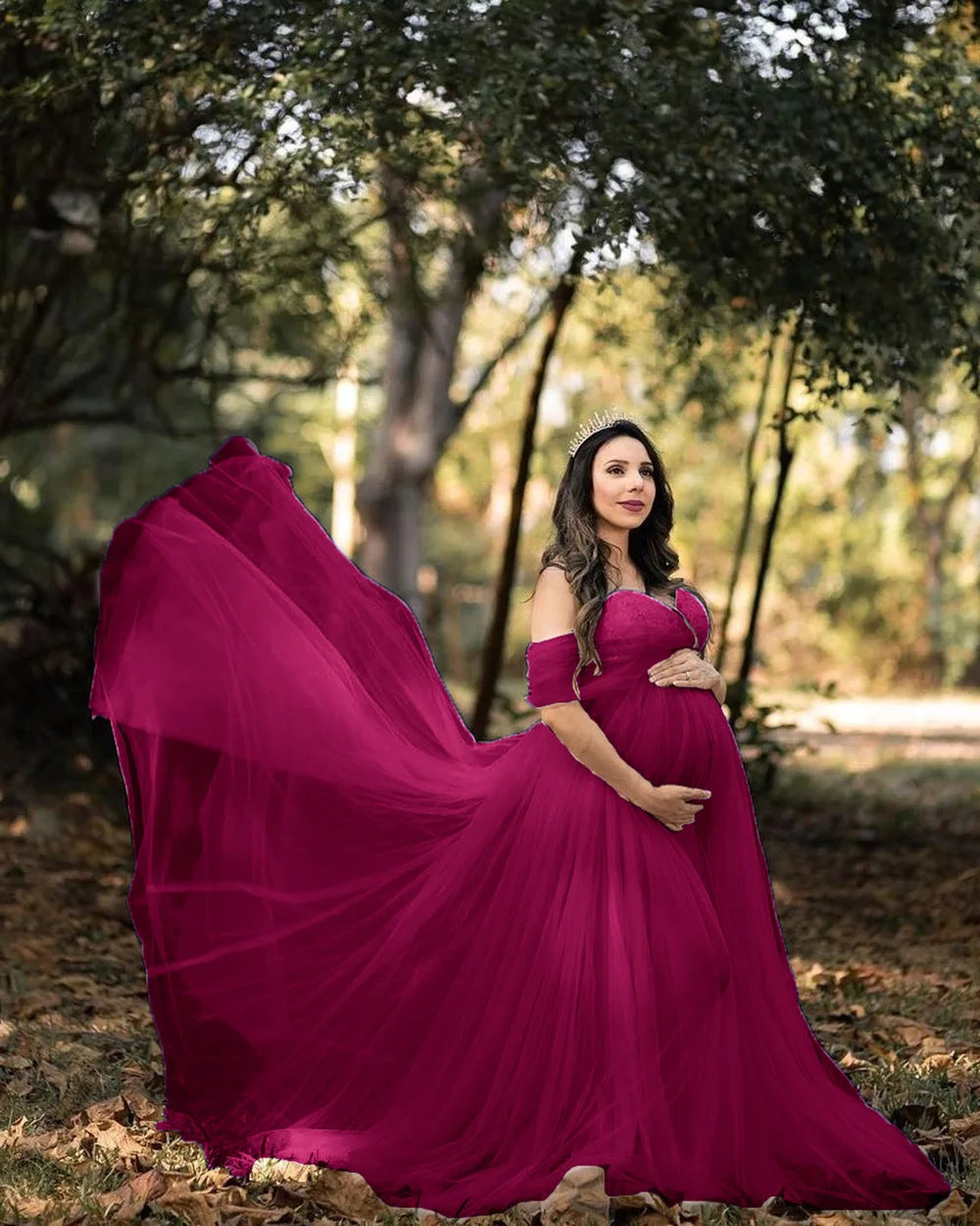 A pregnant woman wears a wine red off-shoulder chiffon maternity gown in a forest setting.