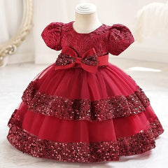 A red short-sleeve party dress for girls featuring a lace bodice, a large bow, and sequin tiers.