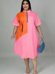 A plus-size woman wears a loose, short-sleeve pink dress with an orange color-blocked panel.