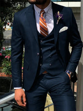 A man wears a dark blue three-piece slim fit suit with a white shirt and an orange striped tie.