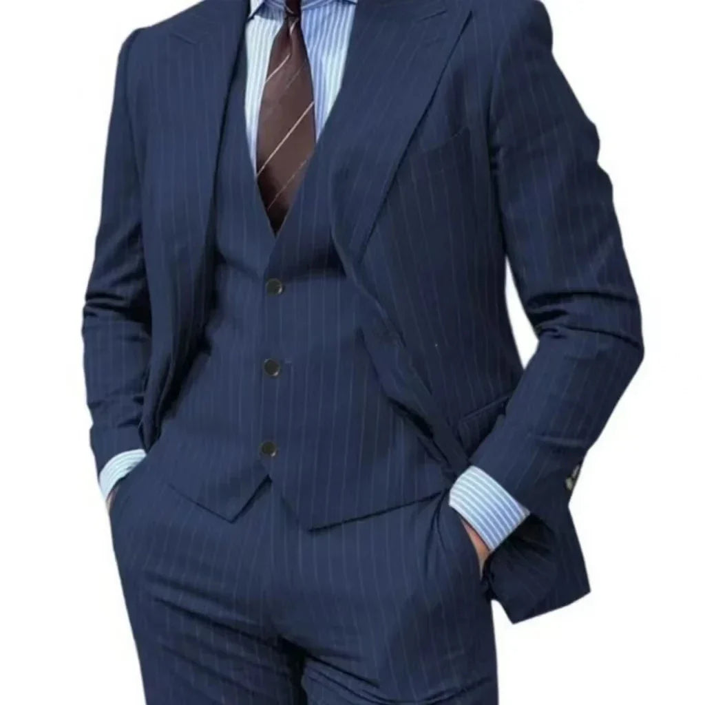 A man wears a navy blue pinstripe three-piece suit with a peak lapel and a striped shirt.