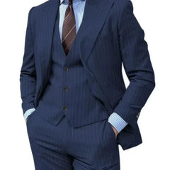 A man wears a navy blue pinstripe three-piece suit with a peak lapel and a striped shirt.