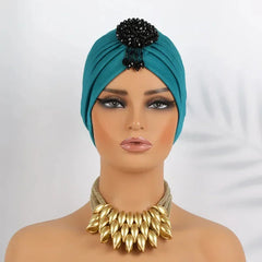 A teal pleated turban headscarf featuring a black beaded embellishment on a mannequin head.