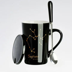 A black ceramic mug featuring a gold Sagittarius constellation, matching lid, and a spoon.