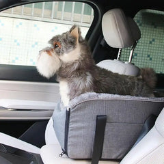 A gray portable pet car seat is secured on a vehicle armrest with a small dog sitting inside.