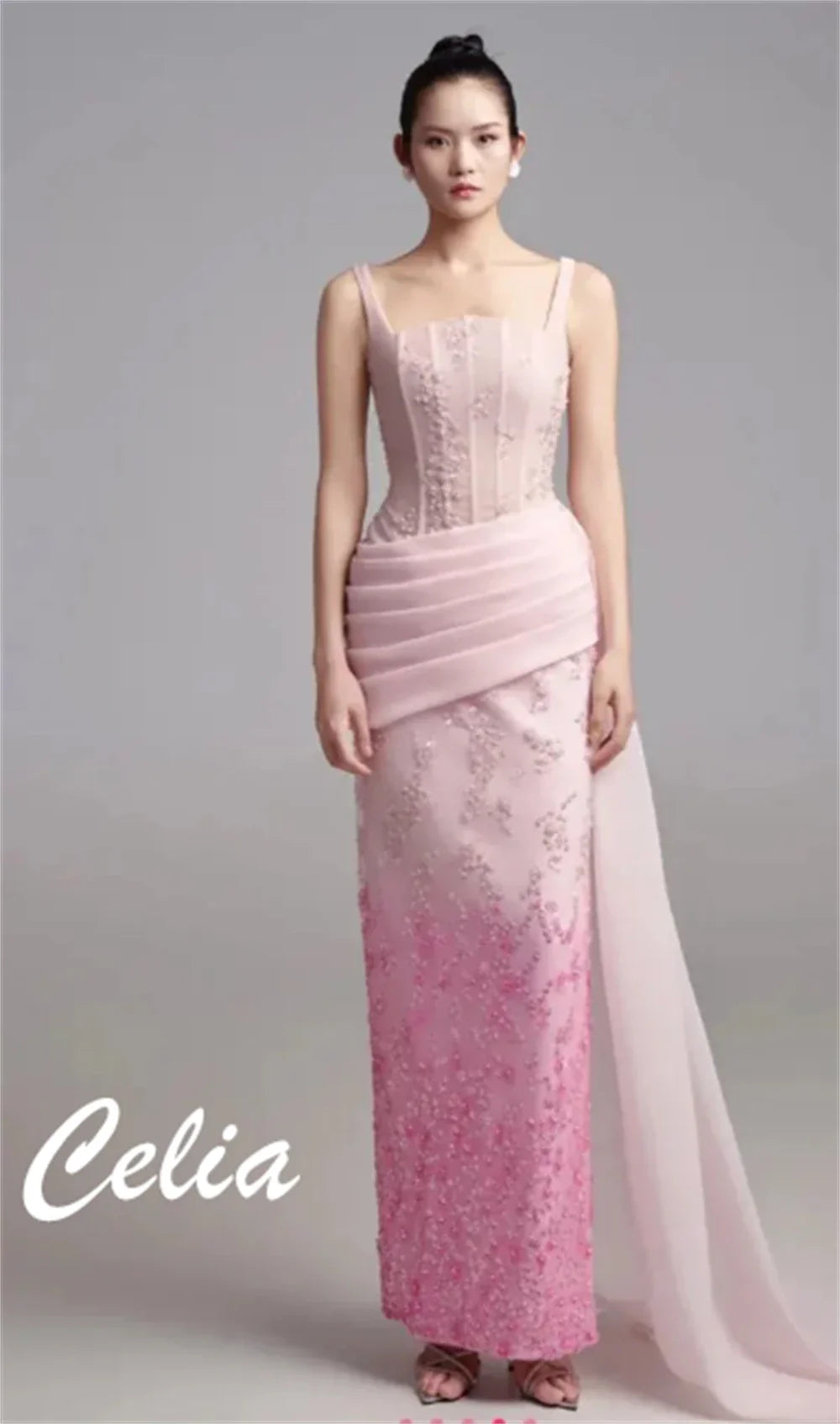 A model wears a floor-length pink satin evening gown with a pleated waist and floral embroidery.