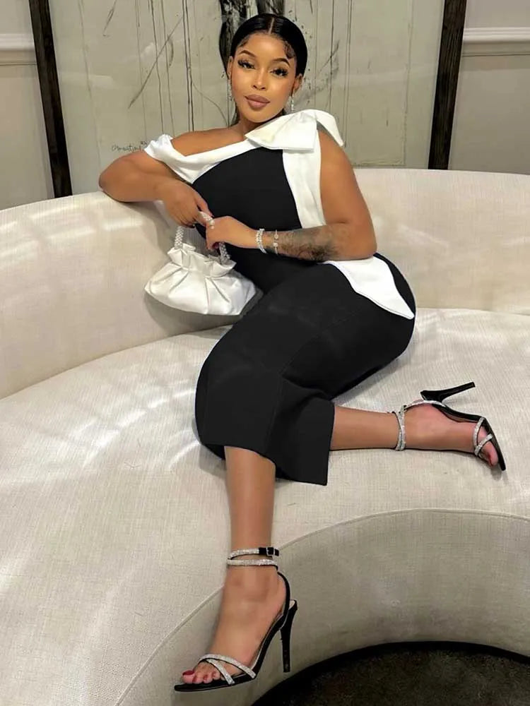 A woman wears a black mid-length dress with a white bow detail on the shoulder.