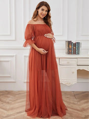 A pregnant woman wears a rust-colored off-shoulder tulle maternity gown with short sleeves.
