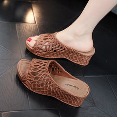 A pair of dark brown wedge slippers featuring a hollow-out woven design and a peep-toe style.
