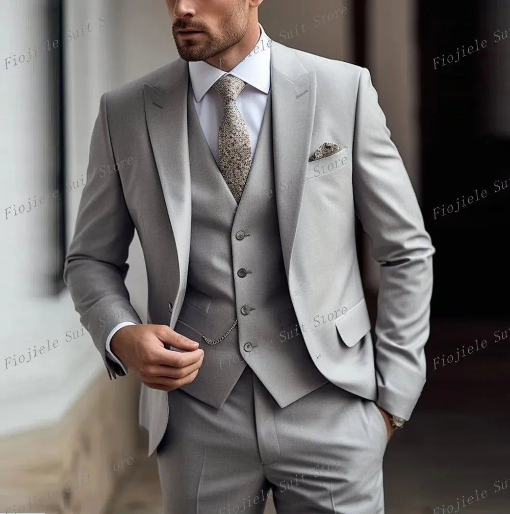 A man wears a light grey three-piece suit with a patterned tie and pocket square.