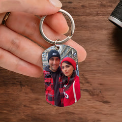 A hand holds a personalized rectangular keychain featuring a photo of a couple wearing beanies.