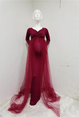 A long-sleeved, ankle-length burgundy maternity dress with a V-neck and a sheer tulle cape train.