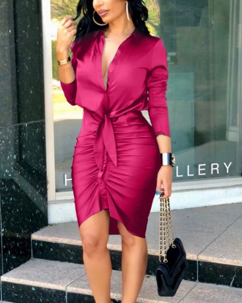 A woman wears a magenta long-sleeve bodycon dress with a deep V-neck and a front tie detail.