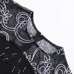A close-up of a black dress featuring a sheer mesh neckline with white floral embroidery and silver beading.